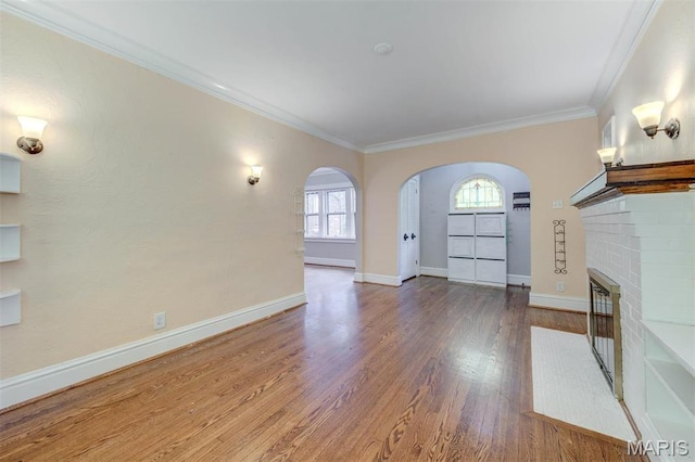 unfurnished living room featuring arched walkways, plenty of natural light, wood finished floors, crown molding, and baseboards