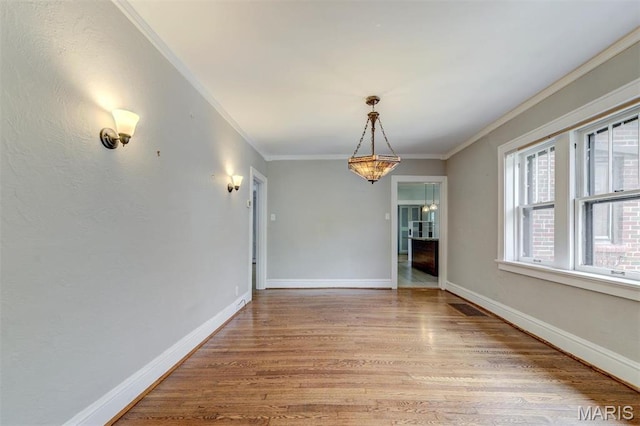 unfurnished dining area featuring crown molding, light wood finished floors, baseboards, and a chandelier