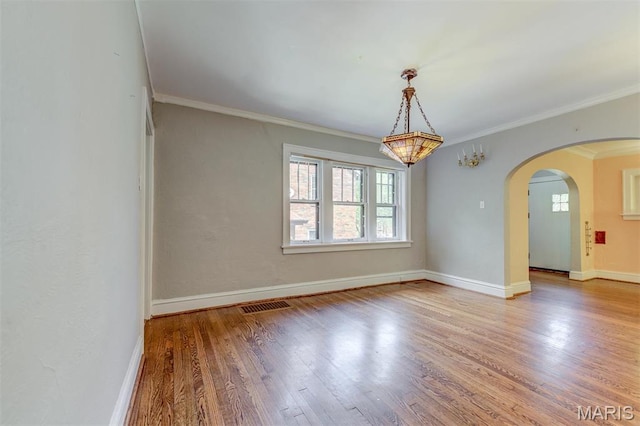 spare room with wood finished floors, baseboards, ornamental molding, and arched walkways