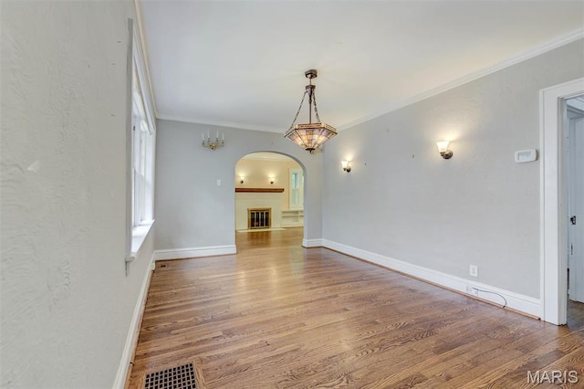 unfurnished dining area with arched walkways, wood finished floors, ornamental molding, and baseboards