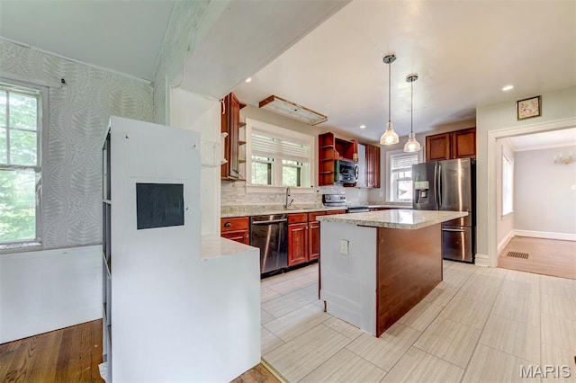kitchen featuring appliances with stainless steel finishes, pendant lighting, a sink, light stone countertops, and a center island