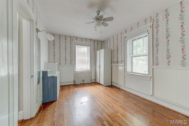 spare room featuring wallpapered walls, wainscoting, healthy amount of natural light, ceiling fan, and light wood-style floors