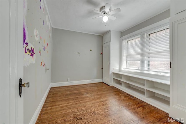 empty room with crown molding, a ceiling fan, wood finished floors, and baseboards