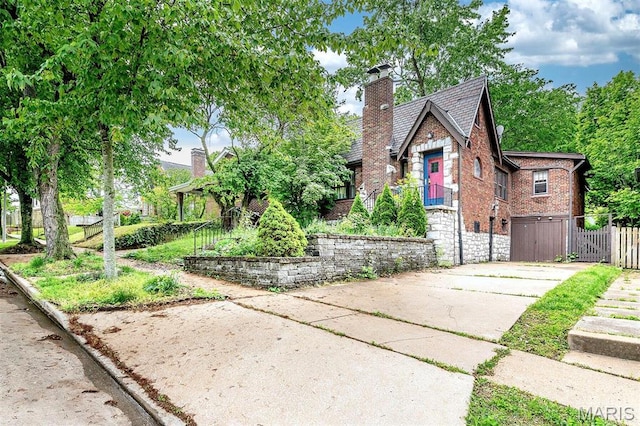 english style home with brick siding, a chimney, stone siding, fence, and concrete driveway