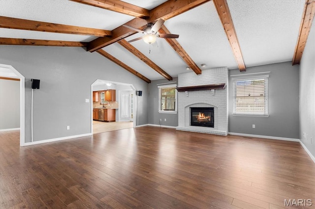unfurnished living room with a ceiling fan, plenty of natural light, a fireplace, and wood finished floors
