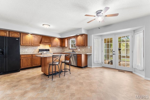 kitchen with stainless steel appliances, french doors, brown cabinets, custom range hood, and decorative backsplash