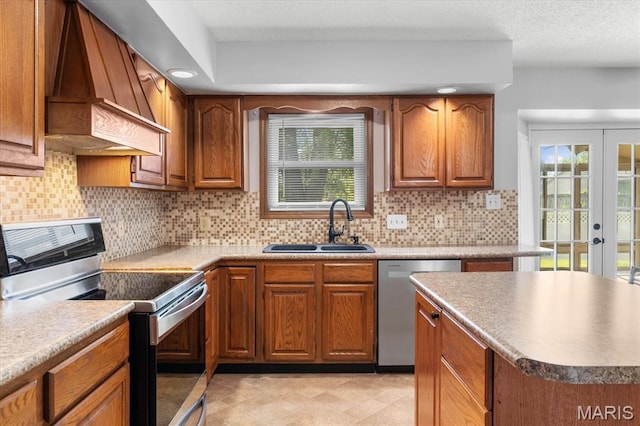 kitchen with appliances with stainless steel finishes, a sink, premium range hood, and brown cabinetry