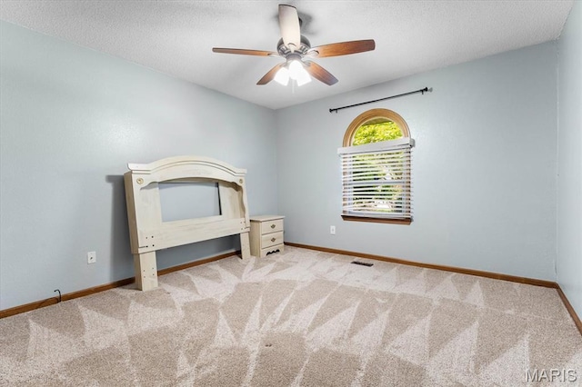 unfurnished bedroom featuring carpet floors, baseboards, a textured ceiling, and a ceiling fan