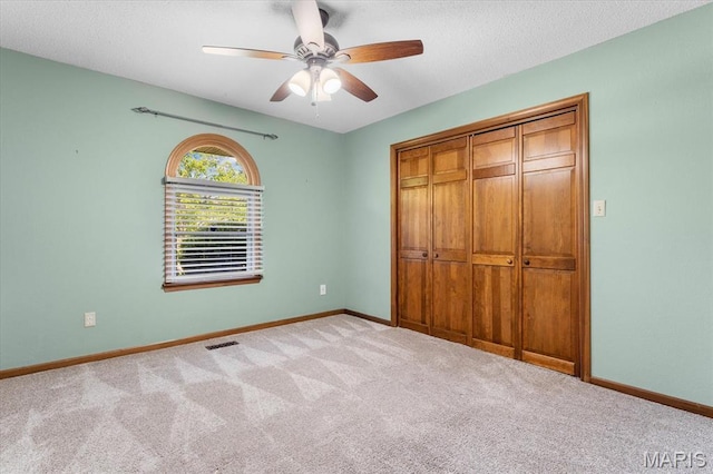 unfurnished bedroom featuring carpet floors, a closet, baseboards, a ceiling fan, and a textured ceiling