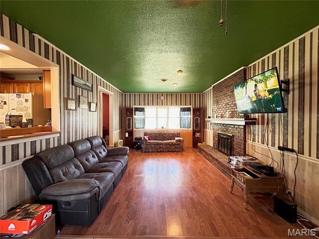 120 E Beth St, Licking, MO 65542 - living room featuring wood finished floors, wallpapered walls, a brick fireplace, and a textured ceiling