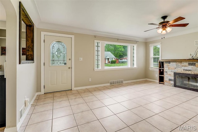 foyer entrance with ceiling fan, a stone fireplace, baseboards, and light tile patterned flooring