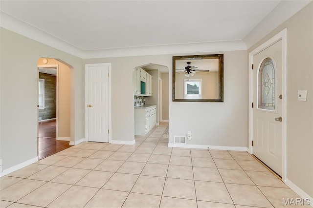 foyer entrance with ceiling fan, arched walkways, light tile patterned floors, and baseboards