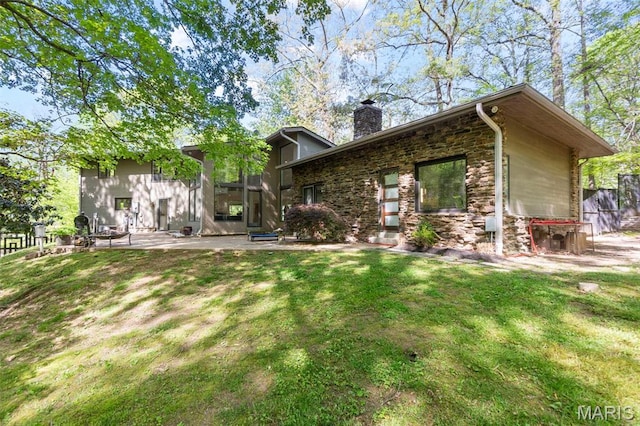 rear view of property with stone siding, a chimney, and a yard