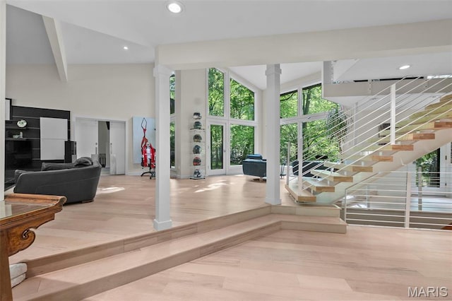 living area featuring wood finished floors, a towering ceiling, recessed lighting, stairway, and ornate columns