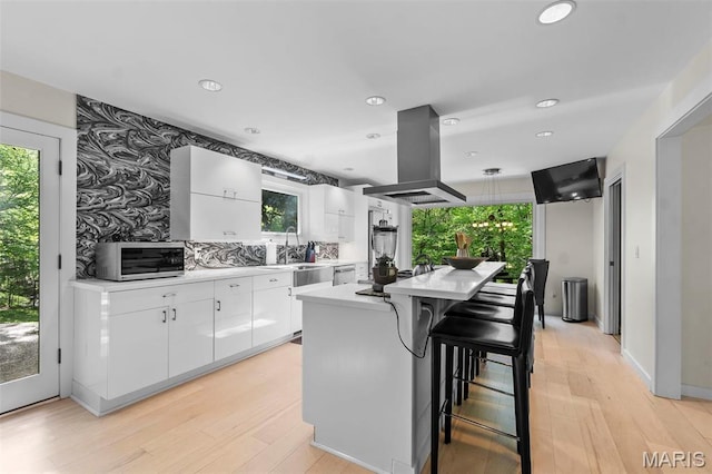 kitchen with island range hood, stainless steel microwave, light countertops, white cabinets, and a center island