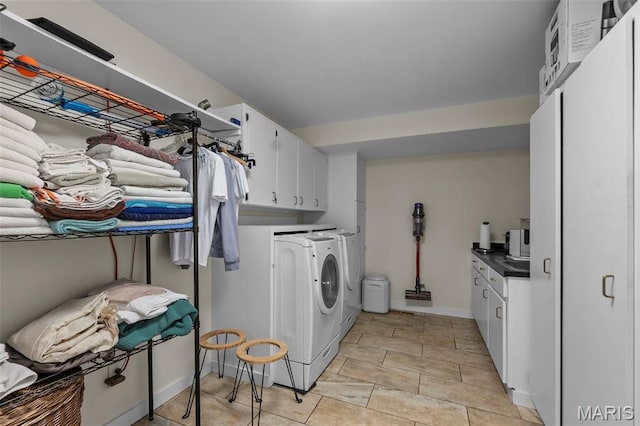 clothes washing area with washing machine and clothes dryer, cabinet space, and baseboards