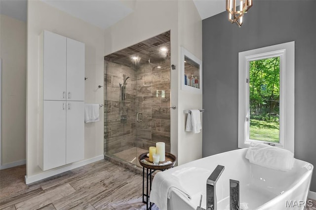 bathroom featuring a stall shower, a soaking tub, a chandelier, wood finished floors, and baseboards