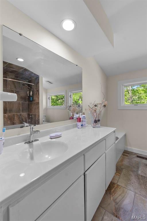 full bath with healthy amount of natural light, stone tile floors, baseboards, and vanity
