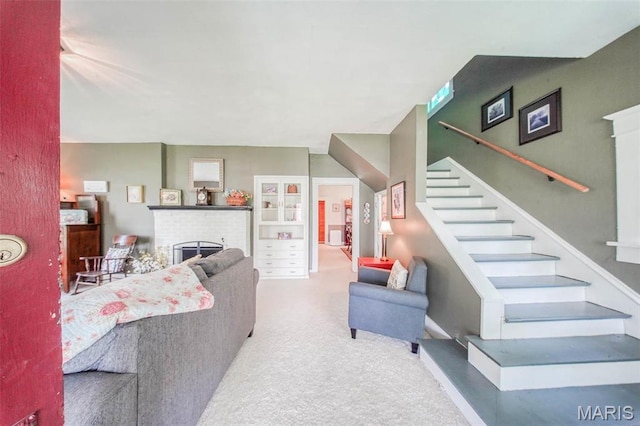 carpeted living room featuring a brick fireplace and stairs