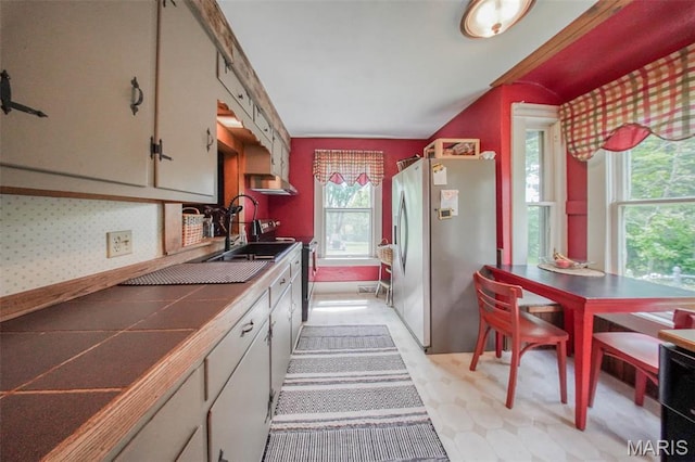 kitchen featuring stainless steel appliances, tile counters, a sink, and light floors