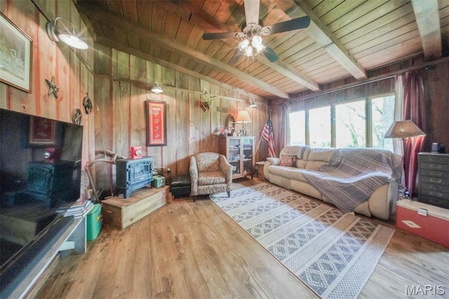 living area featuring wood walls, wood finished floors, ceiling fan, a wood stove, and wood ceiling