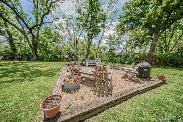 view of green lawn featuring a fire pit and view of scattered trees