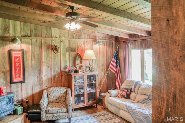 living area featuring wood walls, beamed ceiling, wood finished floors, wood ceiling, and ceiling fan