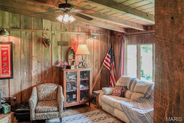 sitting room featuring wood walls, wood ceiling, ceiling fan, beamed ceiling, and wood finished floors