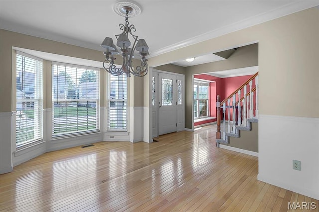 unfurnished dining area featuring a chandelier, hardwood / wood-style floors, crown molding, stairs, and baseboards