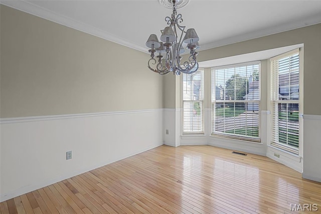 unfurnished room featuring a chandelier, healthy amount of natural light, hardwood / wood-style floors, and crown molding