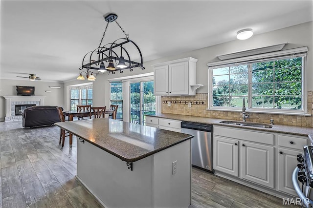 kitchen with dishwasher, a sink, a kitchen island, a brick fireplace, and white cabinets