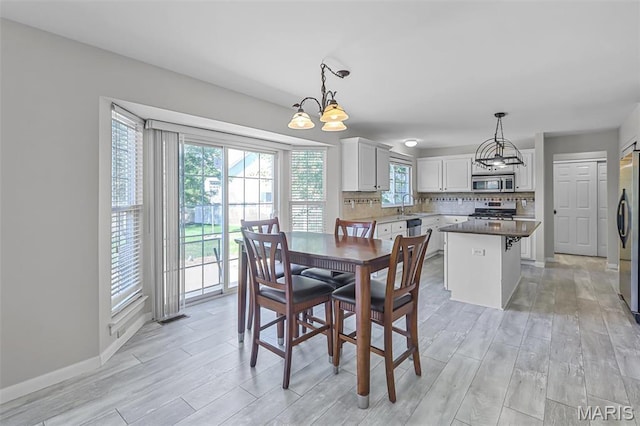 dining room featuring a chandelier, healthy amount of natural light, light wood-style floors, and baseboards