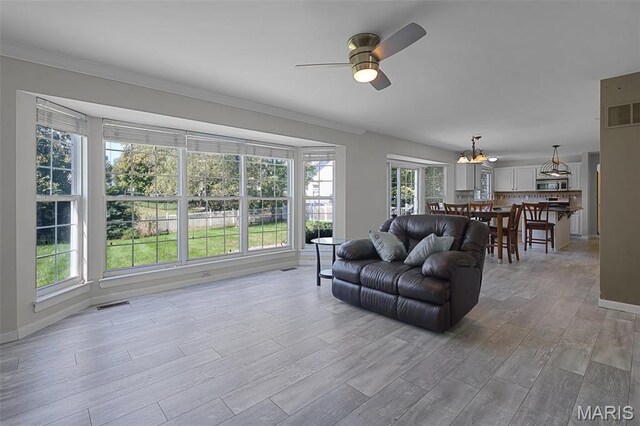 living room featuring a ceiling fan, wood finished floors, a chandelier, baseboards, and ornamental molding