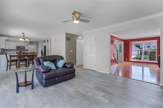living area featuring a ceiling fan, stairs, light wood finished floors, crown molding, and baseboards