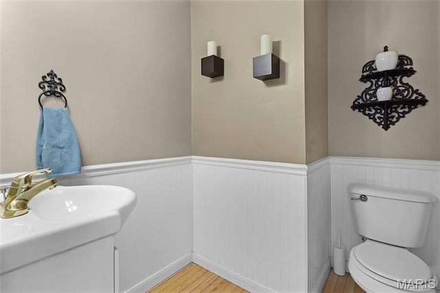 bathroom featuring a wainscoted wall, wood finished floors, toilet, and a sink
