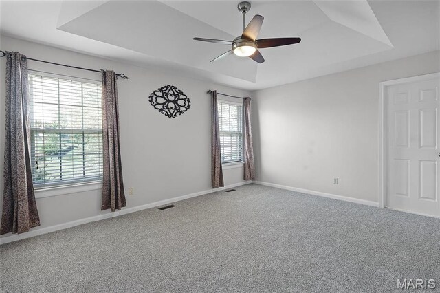 carpeted empty room featuring a raised ceiling, ceiling fan, and baseboards