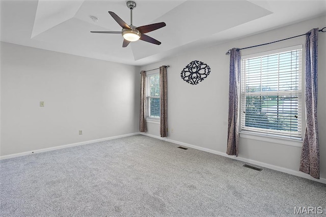 empty room with a raised ceiling, carpet floors, a ceiling fan, and baseboards