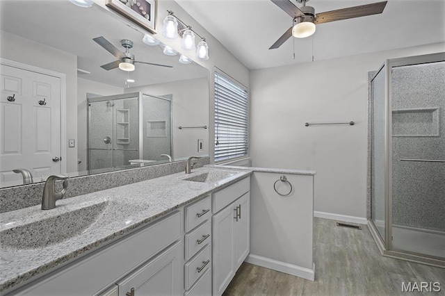 full bath with ceiling fan, wood finished floors, a stall shower, double vanity, and baseboards