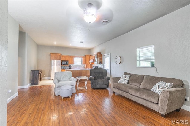 living room featuring wood-type flooring, ceiling fan, baseboards, and a textured wall