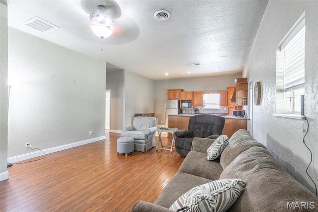 living room featuring a textured wall, wood finished floors, a ceiling fan, baseboards, and a textured ceiling