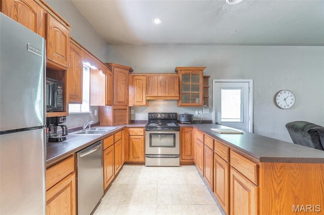 kitchen with appliances with stainless steel finishes, a sink, a peninsula, dark countertops, and glass insert cabinets