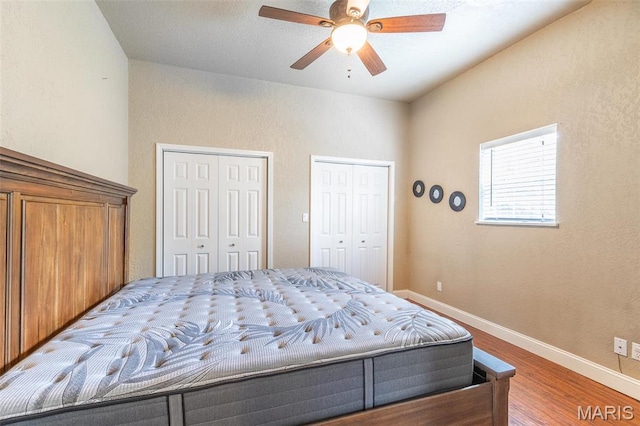 bedroom with two closets, wood finished floors, baseboards, and ceiling fan