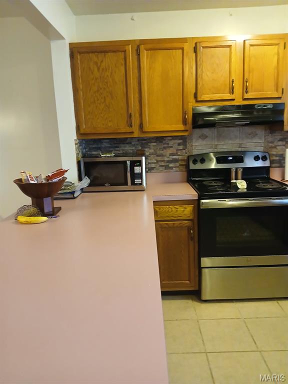 10506 Camden Park Dr, Saint Louis, MO 63135 - kitchen featuring appliances with stainless steel finishes, under cabinet range hood, tasteful backsplash, light countertops, and light tile patterned flooring