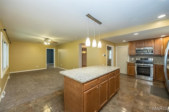 126 E Waymire Ave, Saint Louis, MO 63119 - kitchen with appliances with stainless steel finishes, a ceiling fan, light stone countertops, brown cabinetry, and a kitchen island