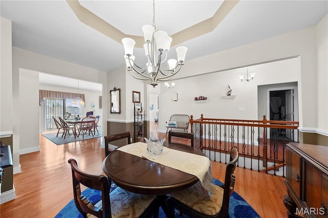 dining room with a chandelier, light wood-style flooring, baseboards, and a raised ceiling