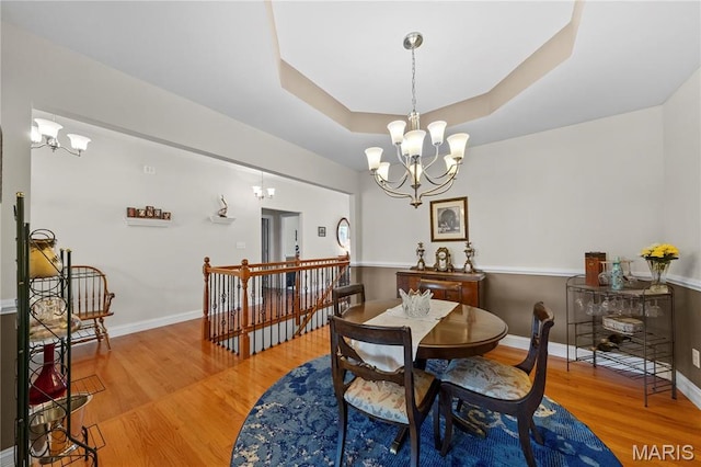 dining area with a chandelier, wood finished floors, a raised ceiling, and baseboards