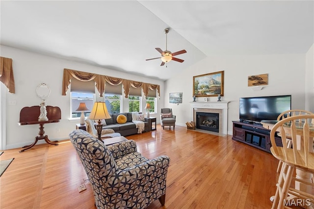 living room featuring a ceiling fan, vaulted ceiling, light wood-type flooring, and a fireplace with flush hearth