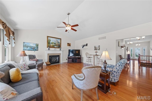 living area featuring ceiling fan, light wood-style floors, lofted ceiling, and a fireplace with flush hearth