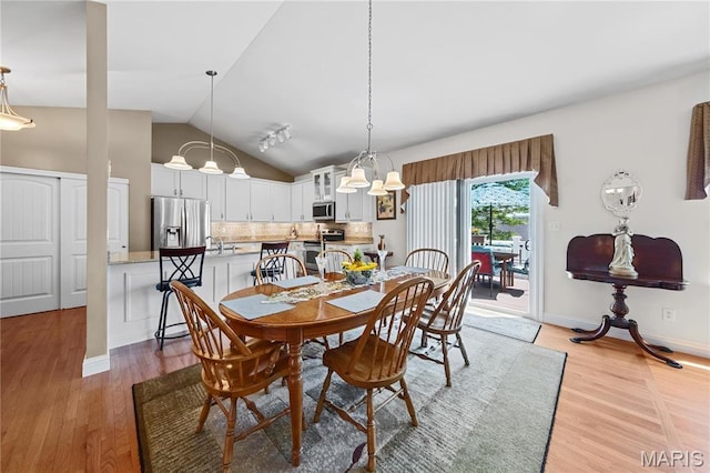 dining area featuring vaulted ceiling, light wood-style flooring, a chandelier, and baseboards