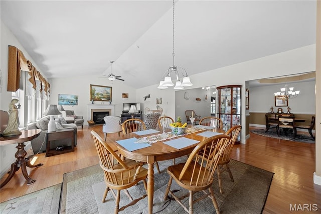 dining area featuring a chandelier, a glass covered fireplace, a ceiling fan, light wood-type flooring, and lofted ceiling